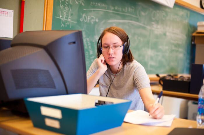 一个年轻女子一边在电脑前听耳机，一边在纸上写字.
